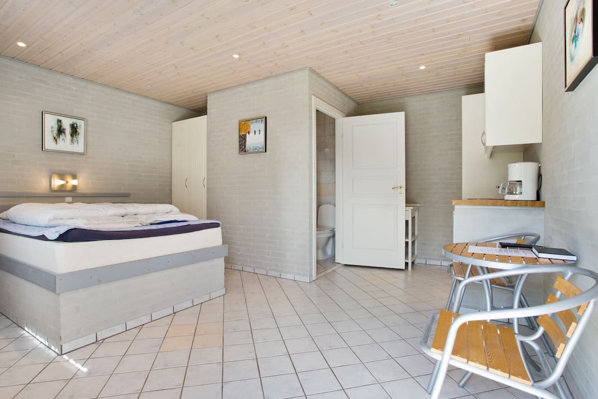 Ein modernes Schlafzimmer mit einem Bett, einem kleinen Tisch und einem Stuhl. Es gibt ein Badezimmer mit Toilette und Waschbecken.