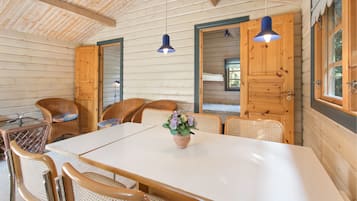Interior de una cabaña de madera con una mesa de comedor, sillas de mimbre y un florero con flores.