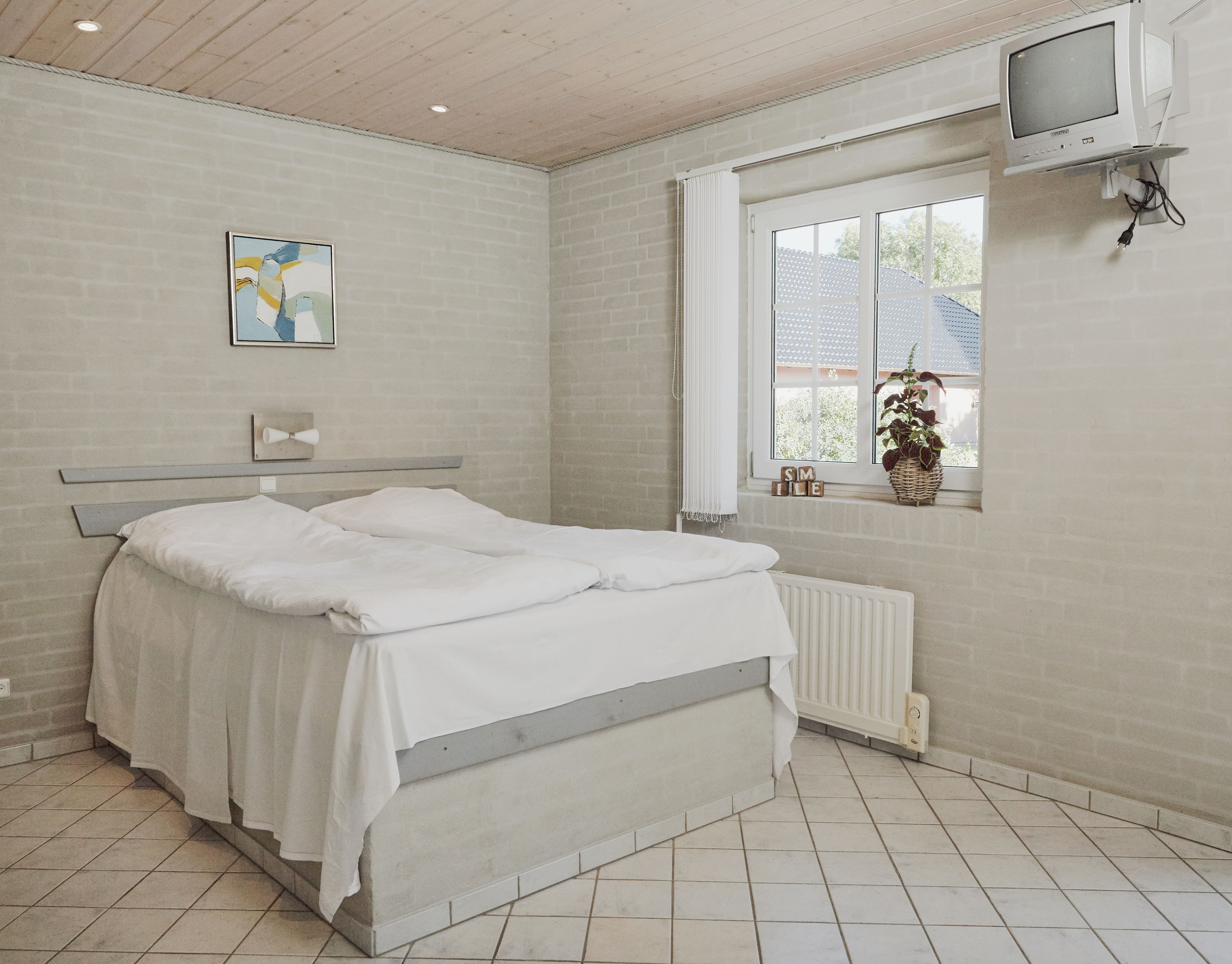A bedroom with a bed, a window, a radiator, and a television.