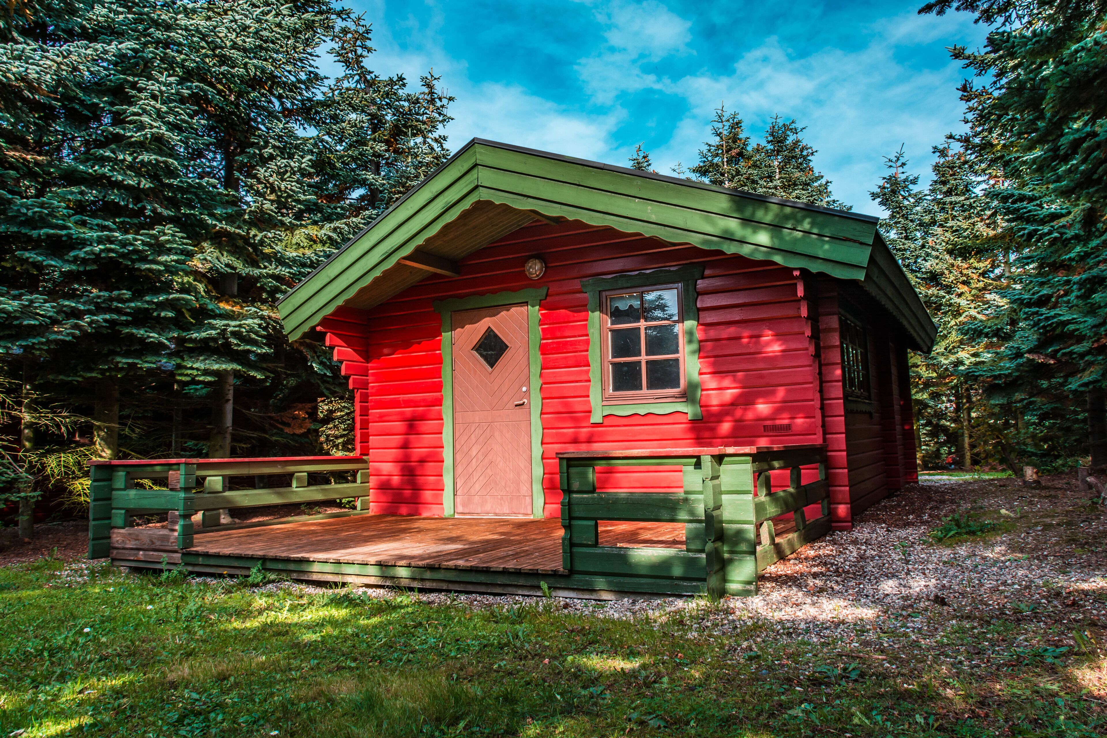 Een klein, rood houten huisje met een groen dak, omringd door bomen.
