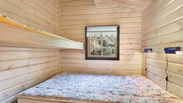 A small wooden cabin room with a bunk bed, a window with a view of trees, and a bed with a patterned blanket.