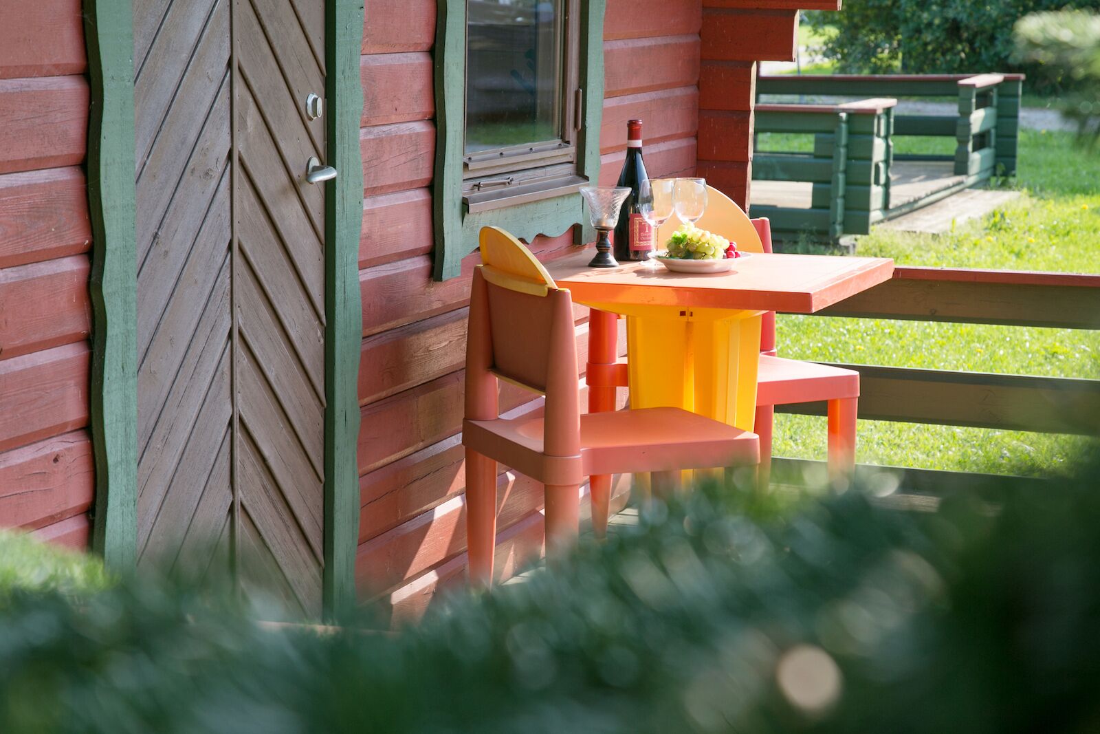 Una cabaña de madera con una mesa de comedor y sillas, una botella de vino y un cuenco de fruta.