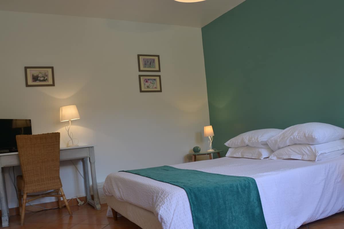 A bedroom with a bed, two bedside tables with lamps, a desk with a chair, and two framed pictures on the wall.
