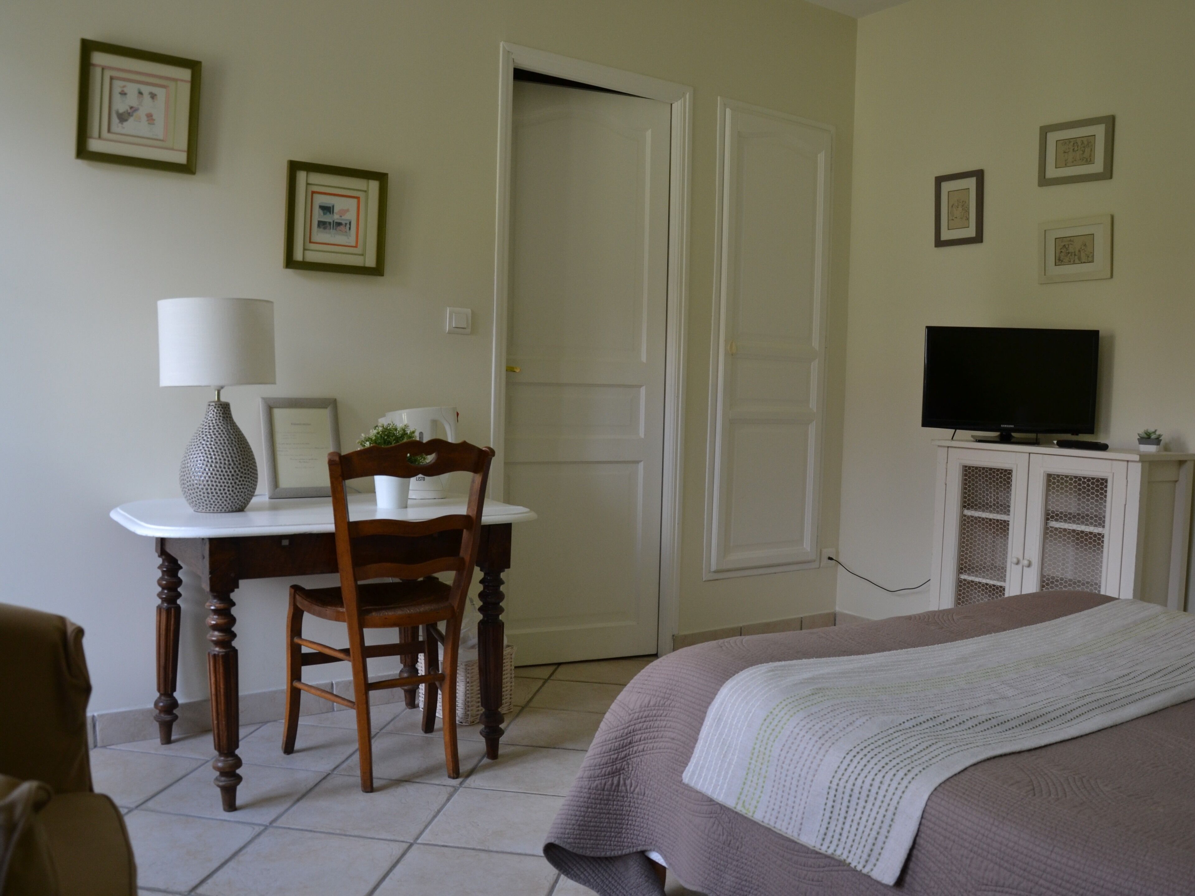 Un dormitorio con cama, un escritorio con silla, televisión y fotografías enmarcadas en la pared.