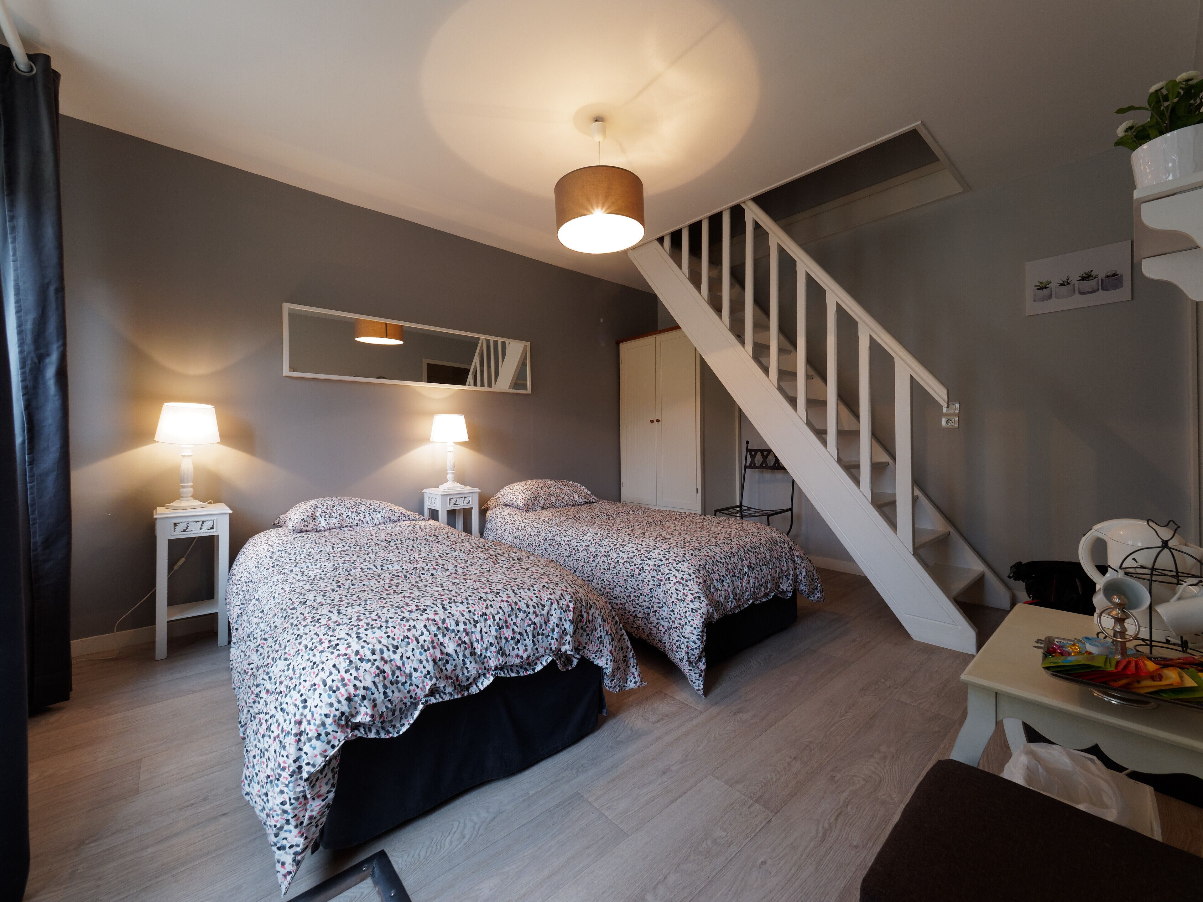 Een slaapkamer met twee bedden, een trap, een spiegel en een kleine tafel met een lamp.