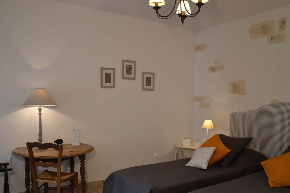 A room with two beds, a dining table, and a chair. There are three framed pictures on the wall.