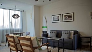 Ett vardagsrum med en soffa, två fåtöljer, ett soffbord och en surfbräda som dekoration.