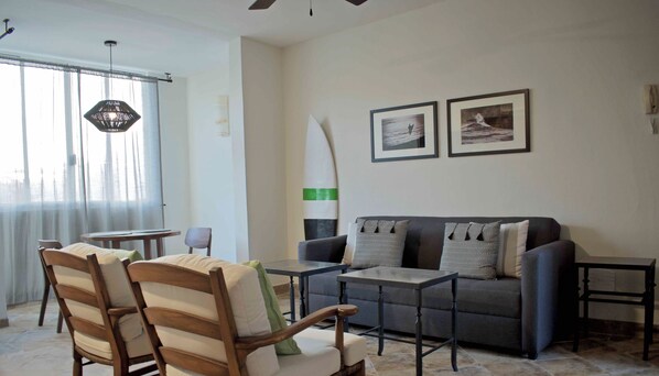 A living room with a sofa, two armchairs, a coffee table, and a surfboard decoration.