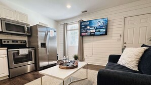 A modern kitchen with stainless steel appliances, a flat-screen TV mounted on the wall, and a cozy living area with a dark sofa and a coffee table. - Private luxury studio- 10 mins downtown and Folly (Charleston County)