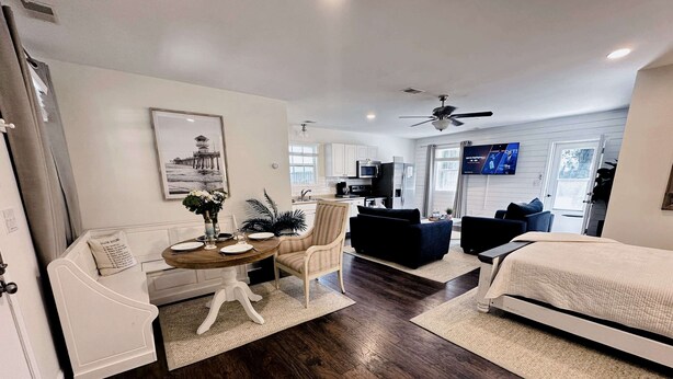 A modern living room with a dining area, dark wooden flooring, white furniture, and a ceiling fan. - Private luxury studio- 10 mins downtown and Folly (Charleston County)