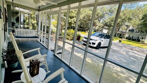 A covered porch with white chairs and a table, large windows offering a view of a street and houses. - Private luxury studio- 10 mins downtown and Folly (Charleston County)