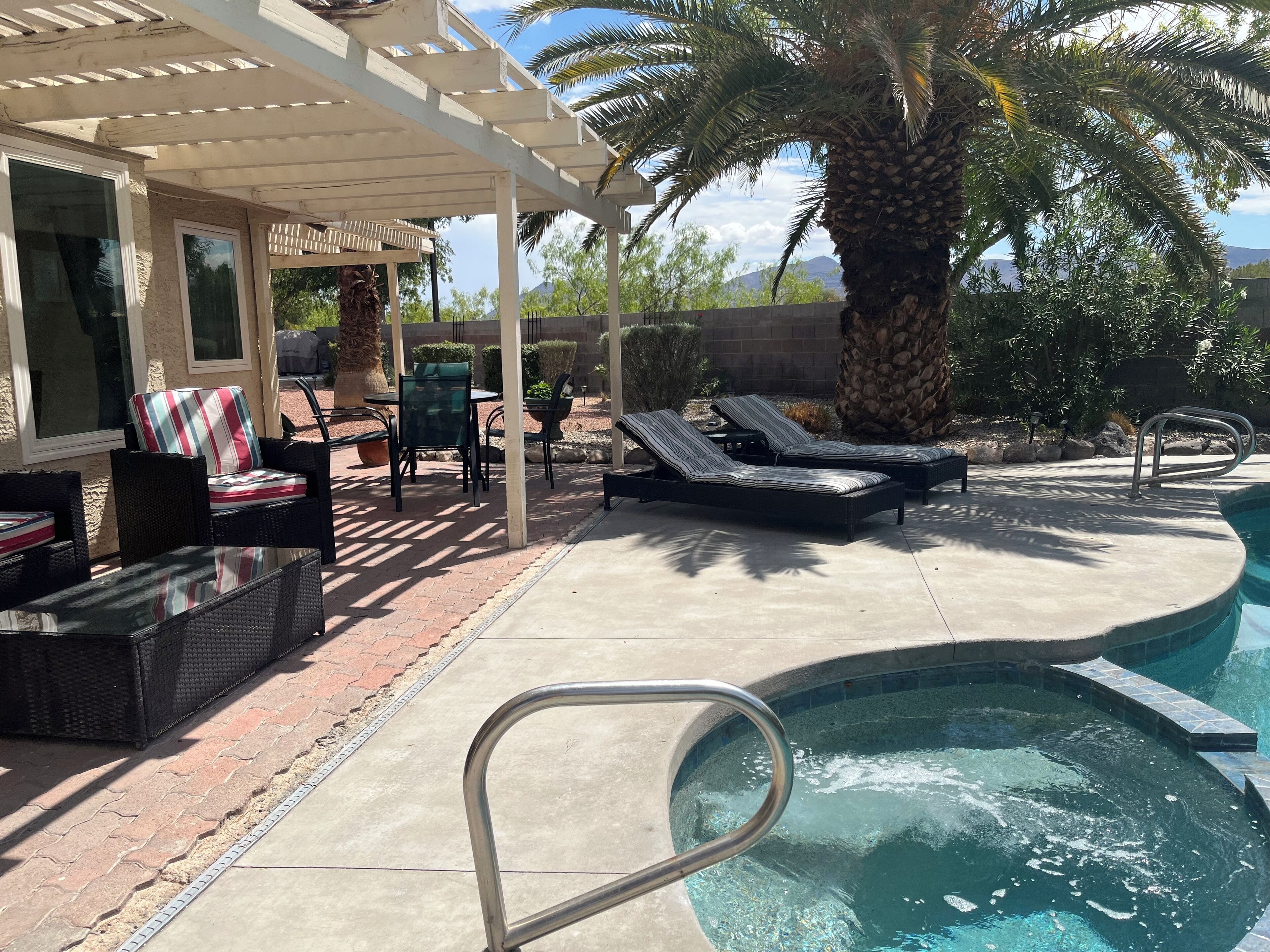 A poolside area with lounge chairs, a pergola, and a view of a mountain.