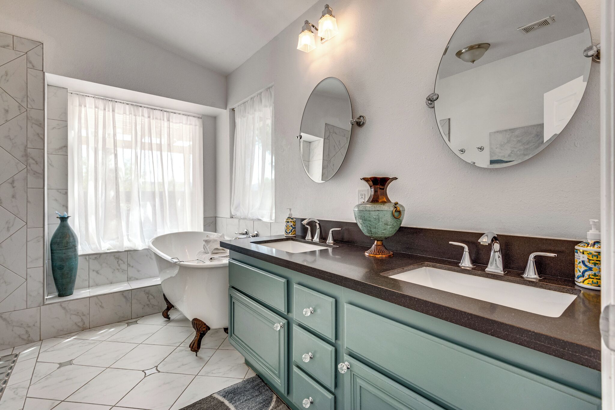 Une salle de bain avec une baignoire sur pieds, deux lavabos, un meuble-lavabo avec des tiroirs et un grand miroir.