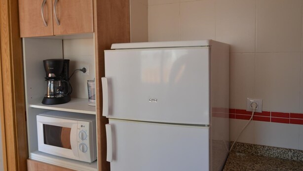 A kitchen with a white refrigerator, a microwave, and a coffee maker on a shelf. - Kione Villamar Habitat (Alcala de Xivert)