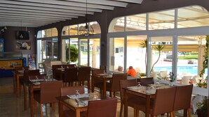 Un restaurant avec des tables et des chaises en bois, de grandes fenêtres et une vue sur une piscine.