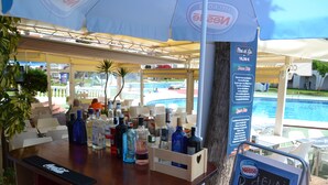 Un espace bar avec vue sur la piscine, un comptoir avec des bouteilles et une enseigne pour Nestle Helados.