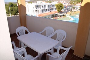 Ein Balkon mit weißem Tisch und Stühlen, mit Blick auf einen Pool und Gebäude.
