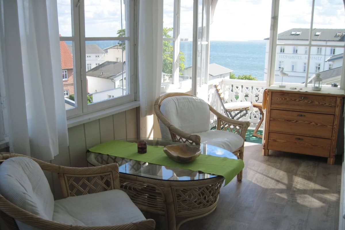 Een balkon met rieten stoelen, een tafel met een groene tafelkleed, en een houten dressoir.