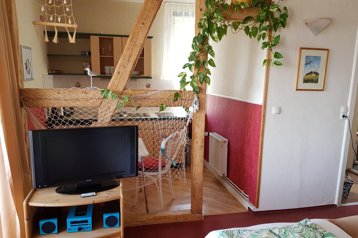 Een gezellige kamer met een televisie op een houten standaard, een klein bureau met elektronische apparaten, een hangmat en een rode en witte muur.