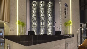 A hotel reception area with a modern design, featuring a reception desk, a decorative wall with geometric patterns, and two potted plants. - SLAVIERO Campina Grande (Campina Grande)