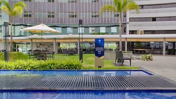 A modern hotel with a pool area, outdoor seating, and a sign indicating the restaurant.