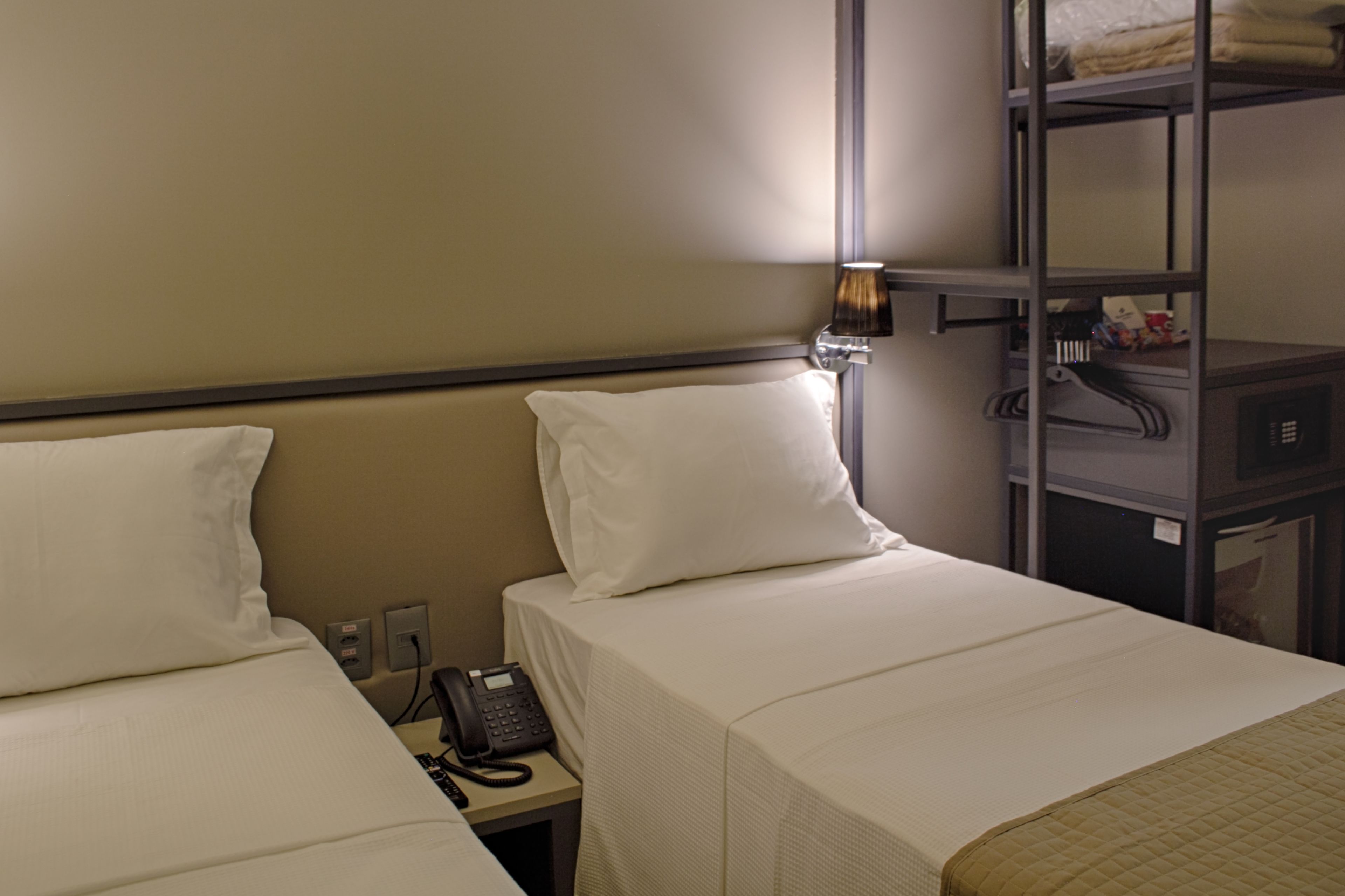 A hotel room with two beds, a bedside phone, and a shelf with folded clothes.