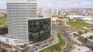 A modern hotel with a curved glass facade, surrounded by a parking area and a busy road. - SLAVIERO Campina Grande (Campina Grande)