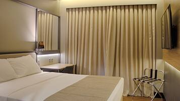 A hotel room with a bed, bedside table, chair, and curtains.