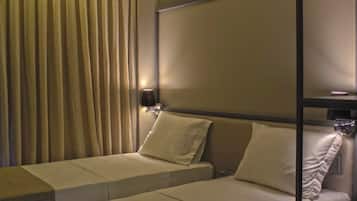 Quarto de hotel com duas camas de solteiro, uma cortina, uma luminária fixada na parede e uma mesa de cabeceira.
