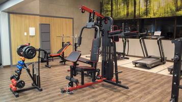 Una palestra dotata di diverse attrezzature per l'allenamento, tra cui una panca per squat, una pressa per bilanciere e tapis roulant.