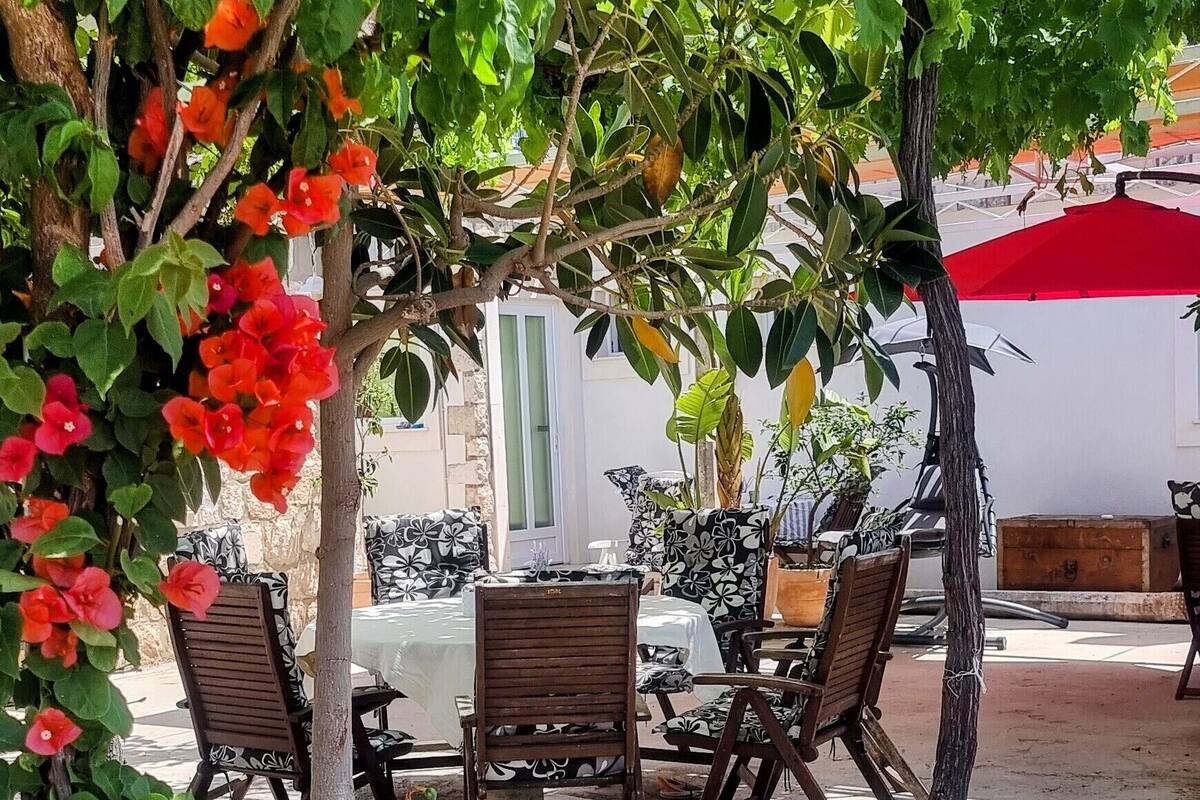 Espaço ao ar livre com mesa e cadeiras sob uma pérgola coberta por trepadeiras floridas.