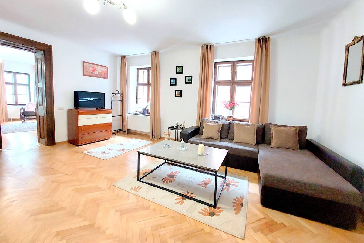 A living room with a sofa, a coffee table, a TV, and a window with curtains.