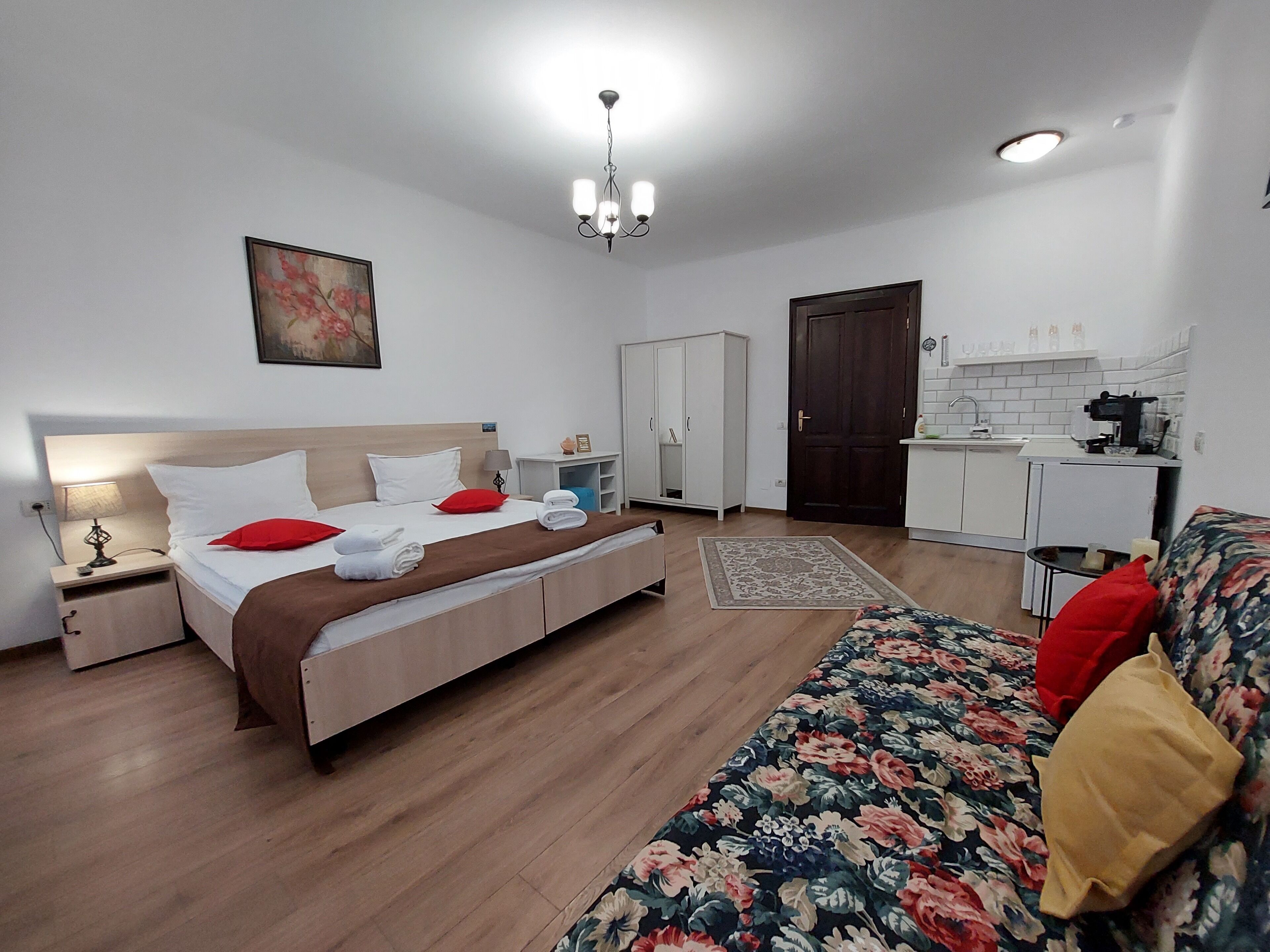 A hotel room with a bed, a sofa, a desk, a wardrobe, and a kitchenette.