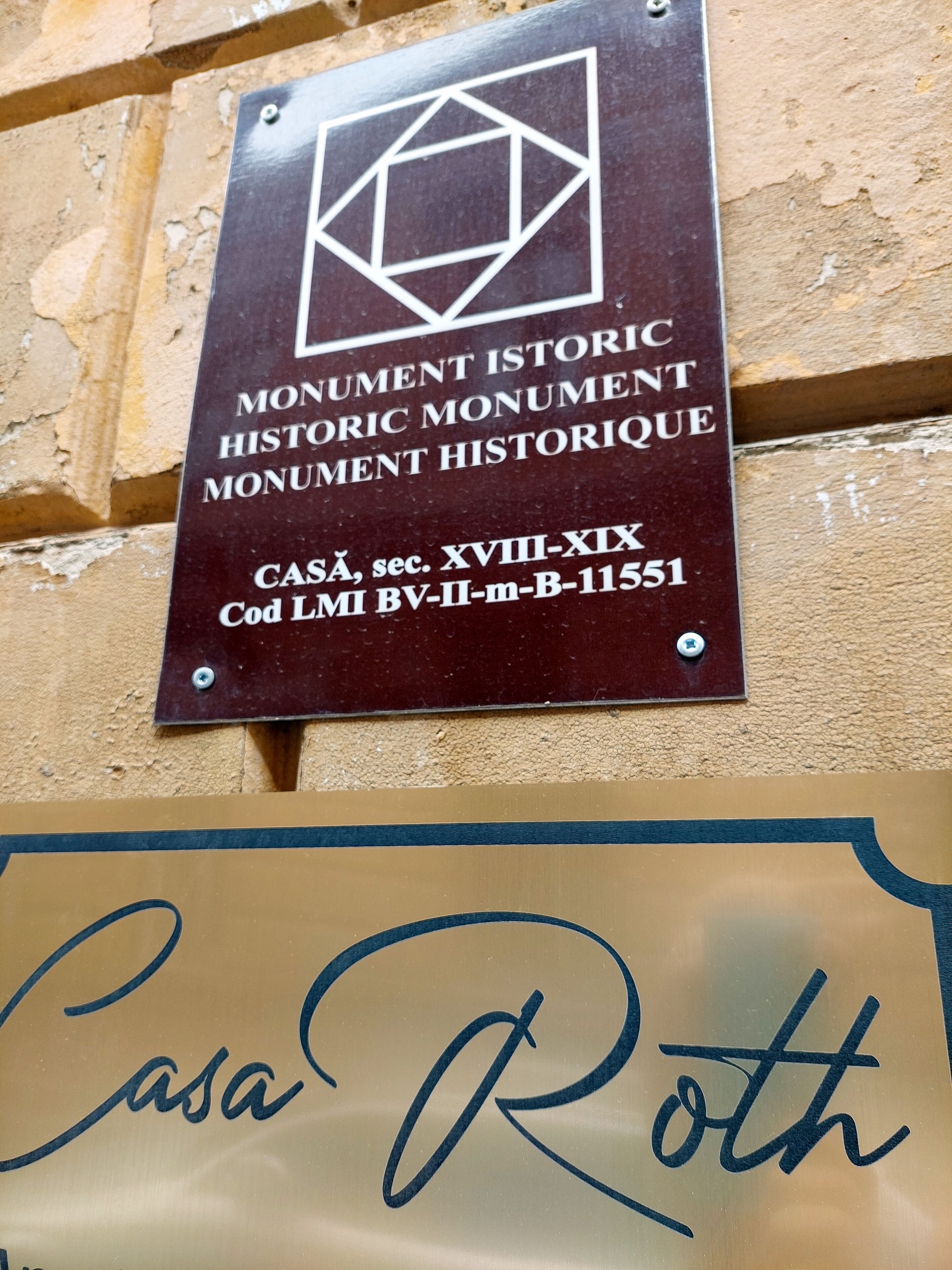 Een plaquette met de tekst 'Monument Historic Monument Historique Monument Historique' en een referentienummer. Daaronder een bordje met 'Casa Roth'.