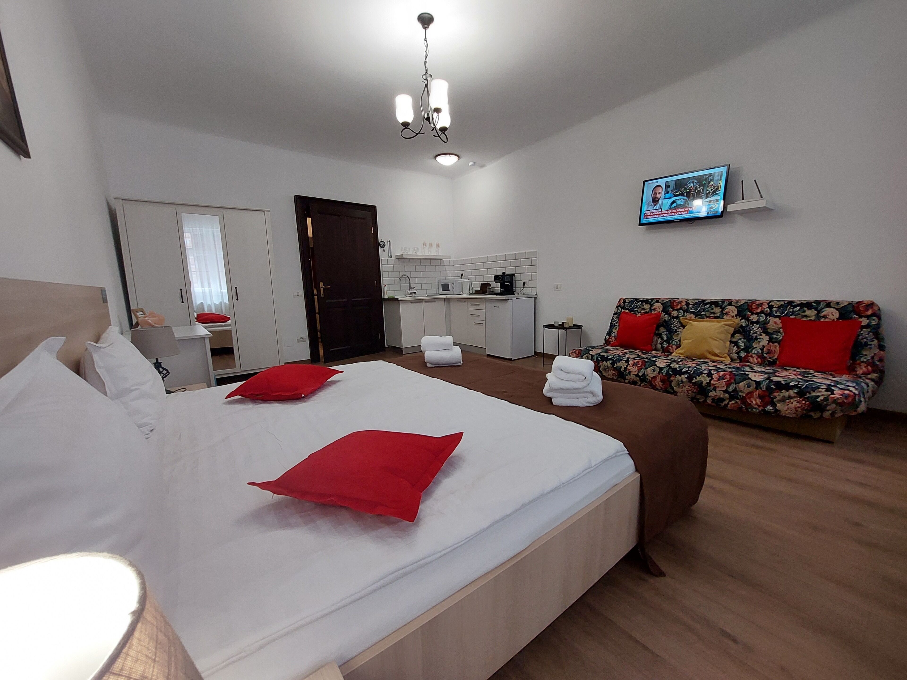 A hotel room with a bed, a sofa, a television, a kitchenette, and a bathroom.