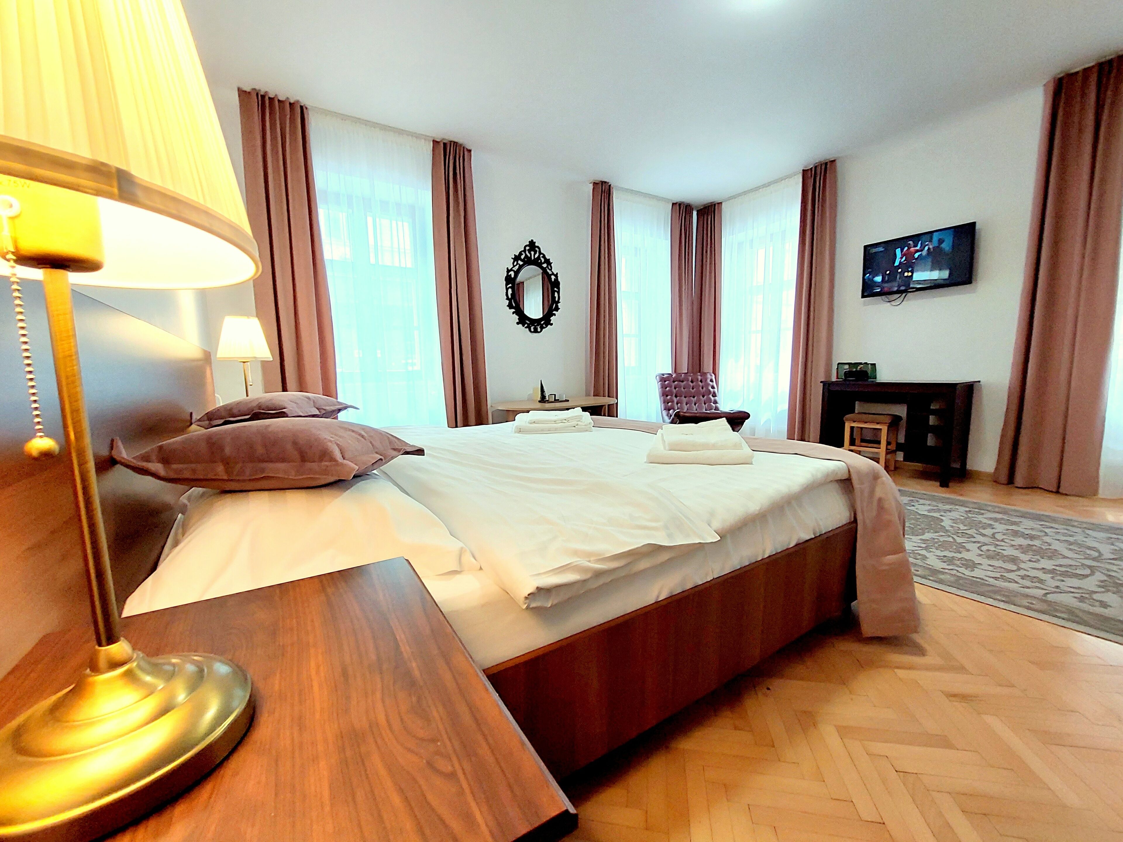 A hotel room with a large bed, a wooden nightstand, a TV, and a fireplace.