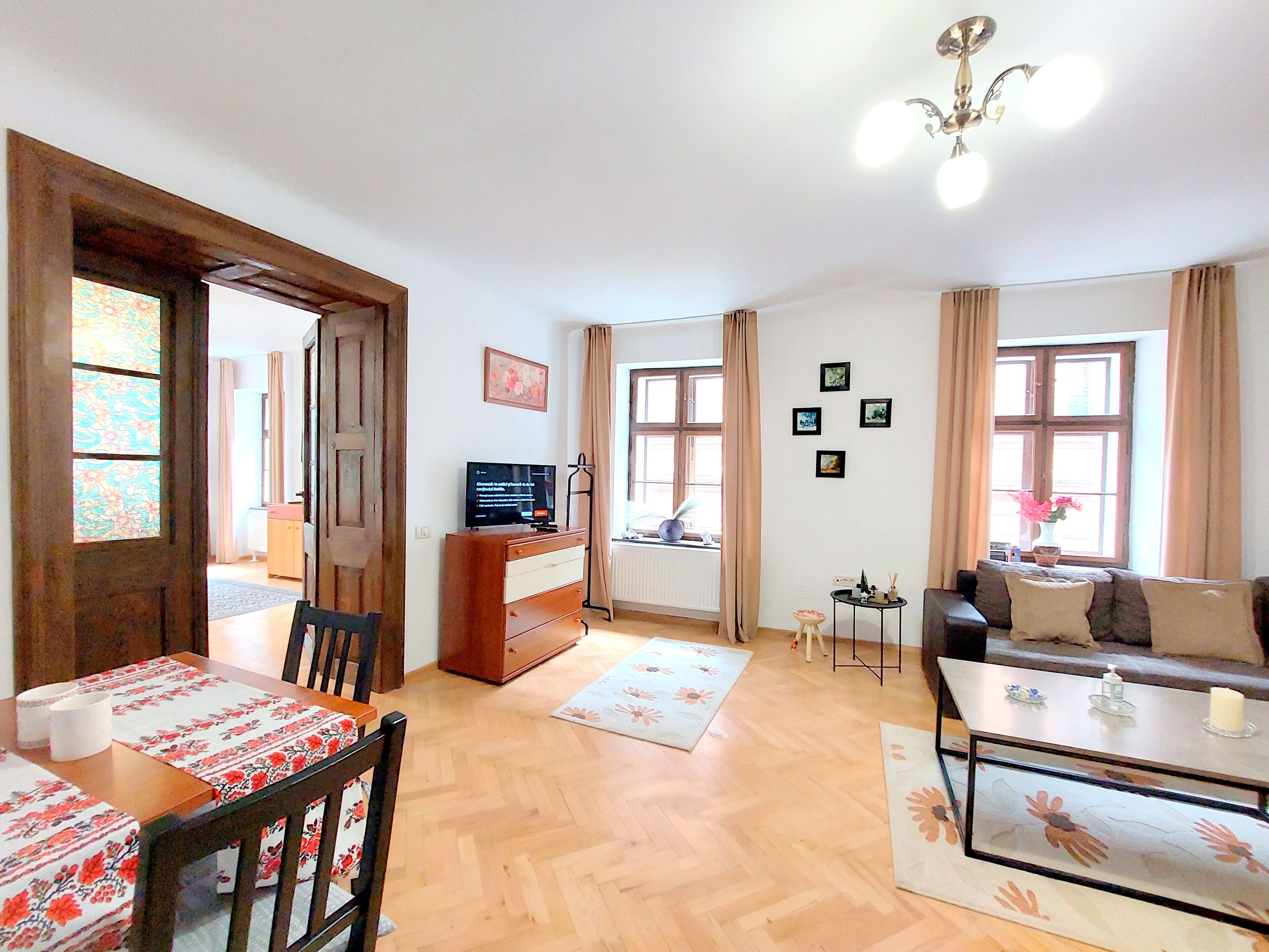 A living room with a wooden floor, a sofa, a coffee table, a TV, and a dining area with chairs and a table.