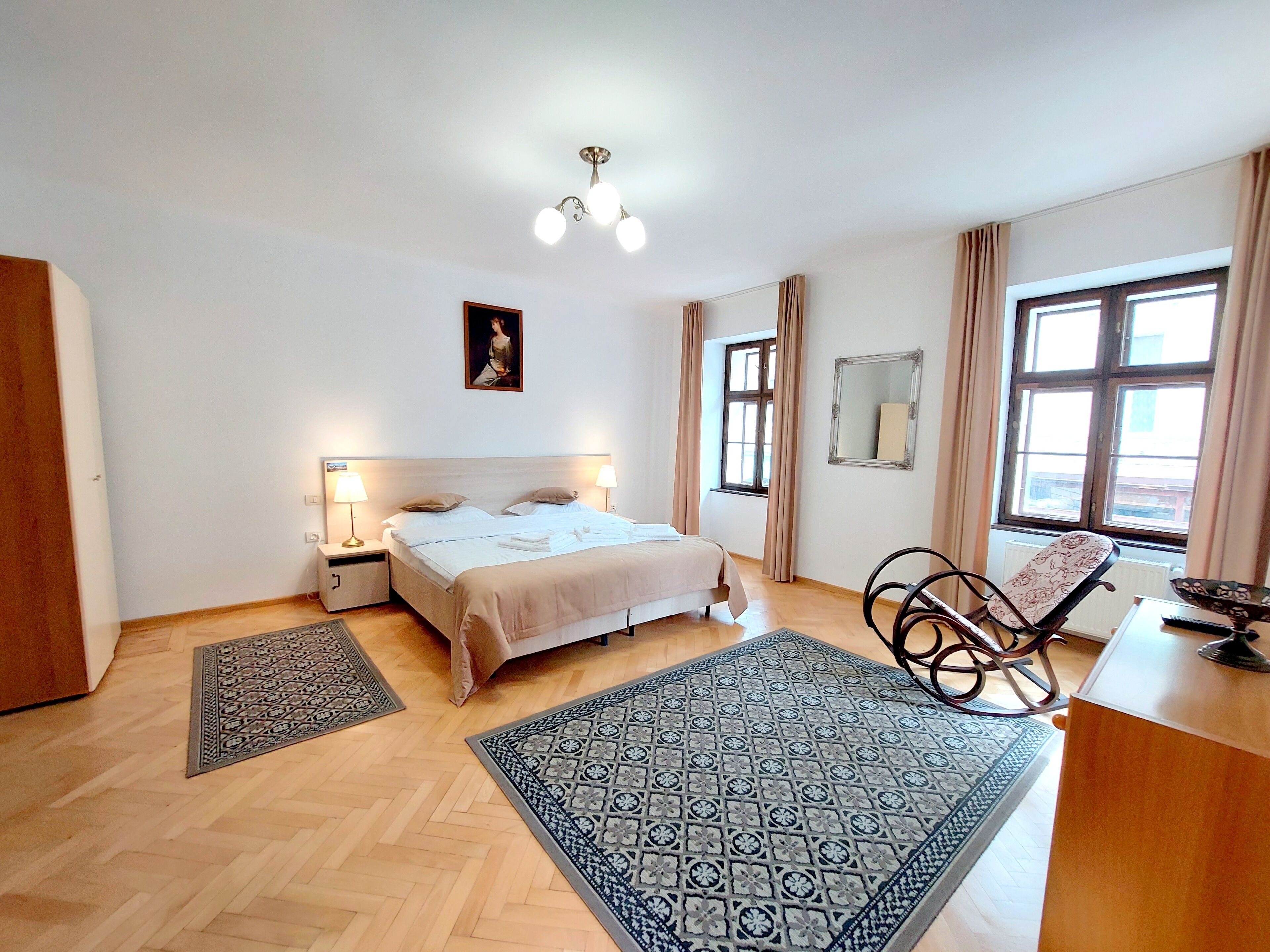 A hotel room with a bed, bedside lamps, a mirror, a chair, and a window.