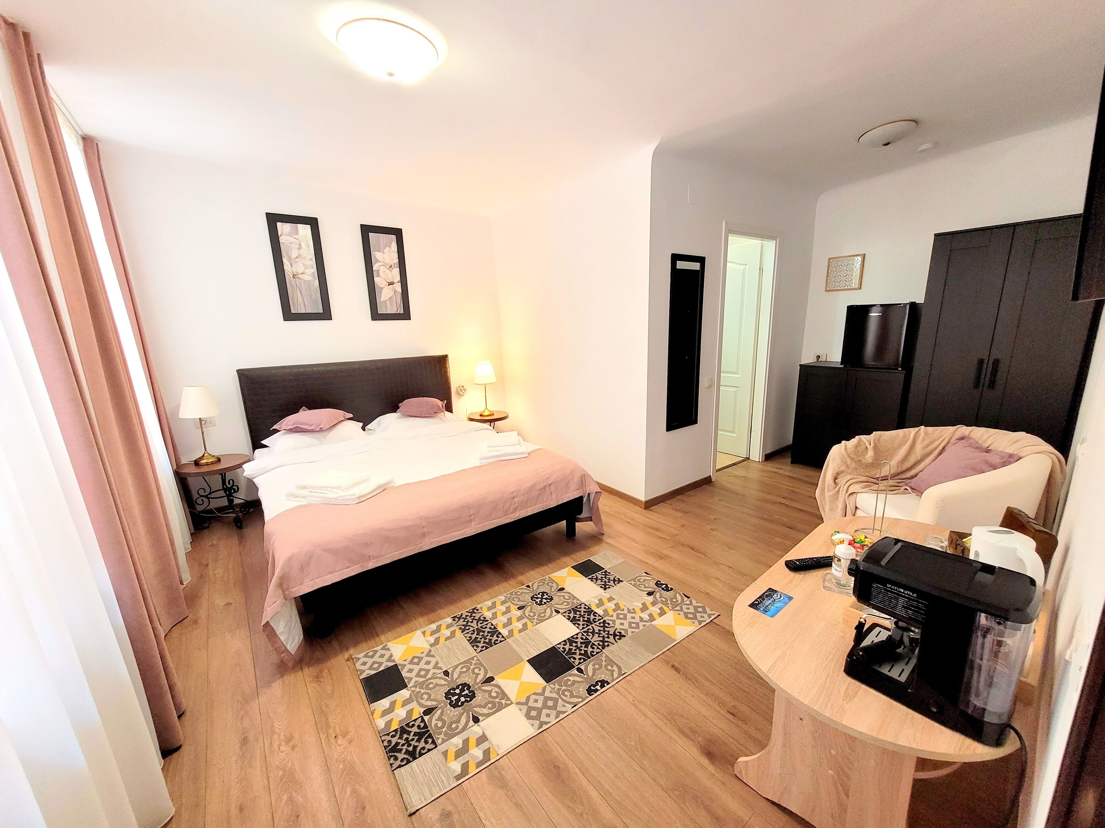 Una habitación de hotel con cama, mesita de noche, lámpara y una cafetera sobre una mesa de madera.