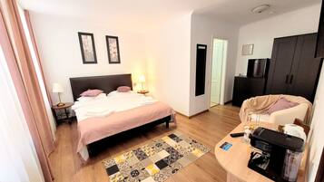 A hotel room with a bed, bedside table, lamp, and a coffee machine on a wooden table.