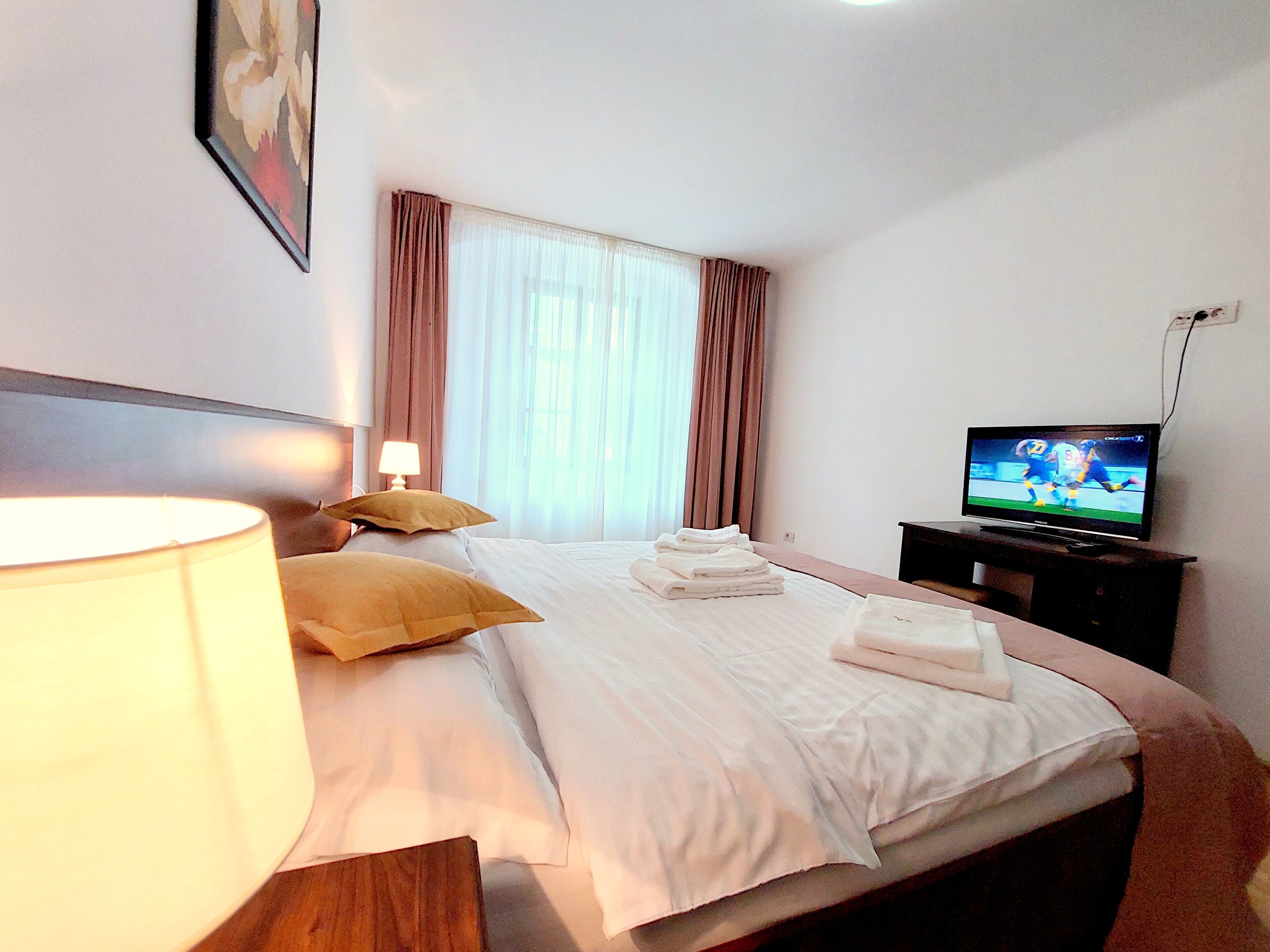 Ein Hotelzimmer mit einem Bett, einem Fernseher, einer Lampe und einem Fenster mit Vorhängen.