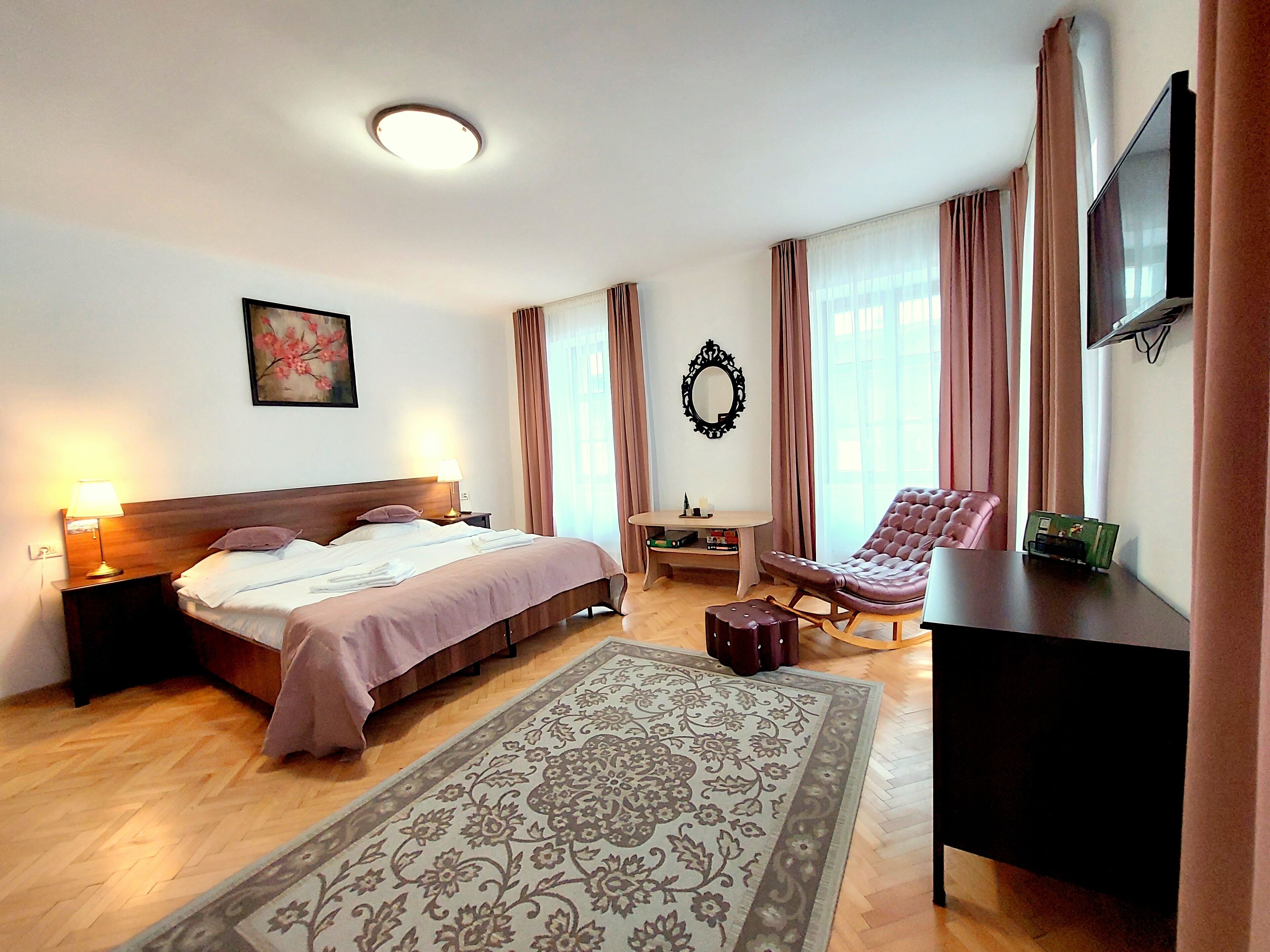 A hotel room with a bed, a desk, a chair, a TV, and a large window with curtains.