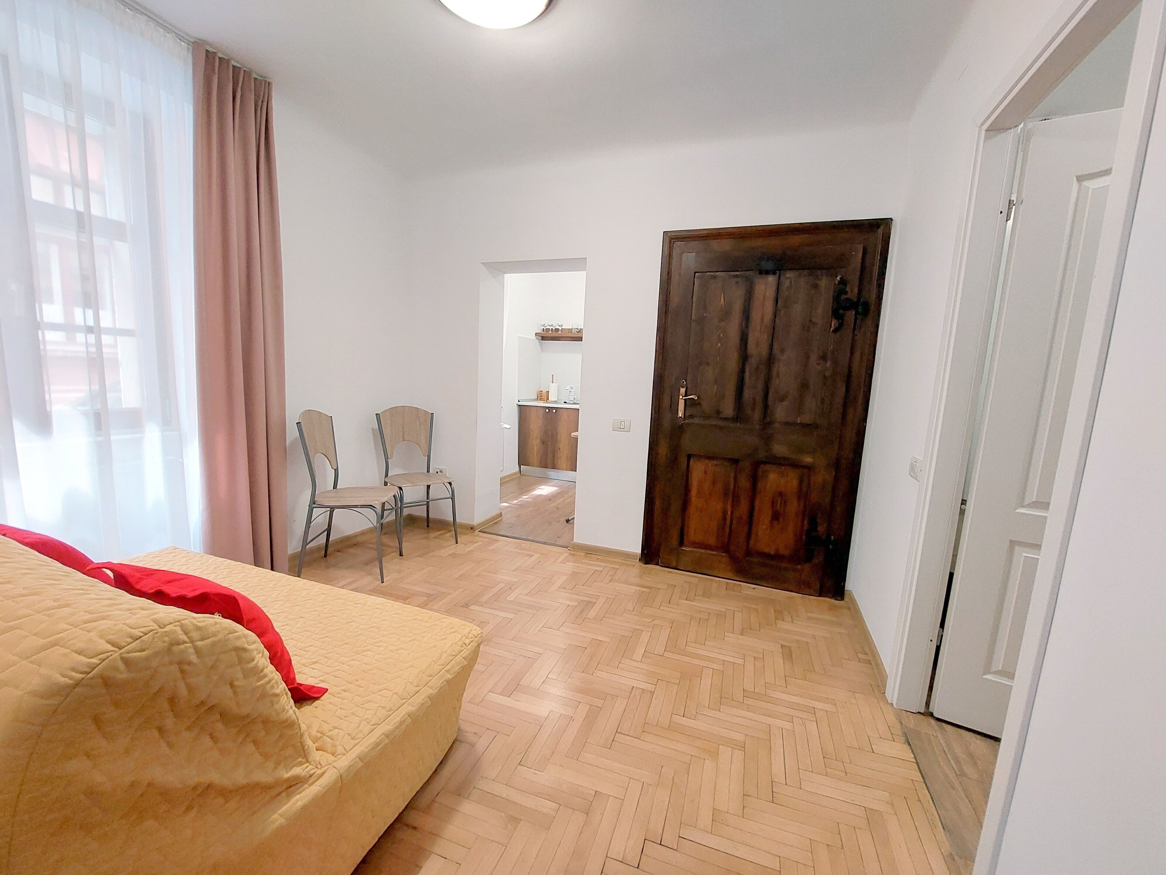 Un dormitorio con una cama, suelo de madera, una puerta y una silla.