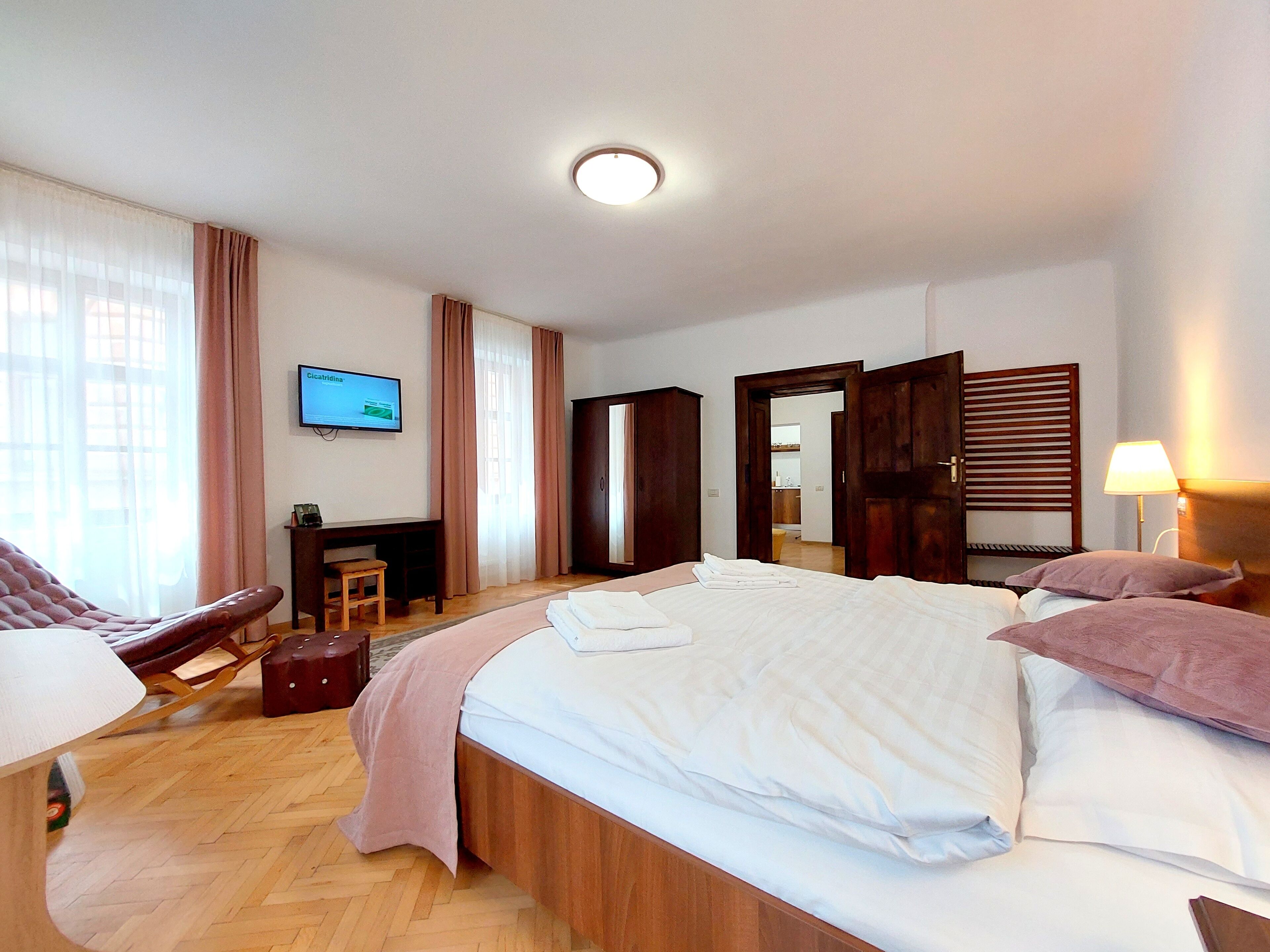 A hotel room with a bed, a desk, a chair, a television, and a wardrobe.