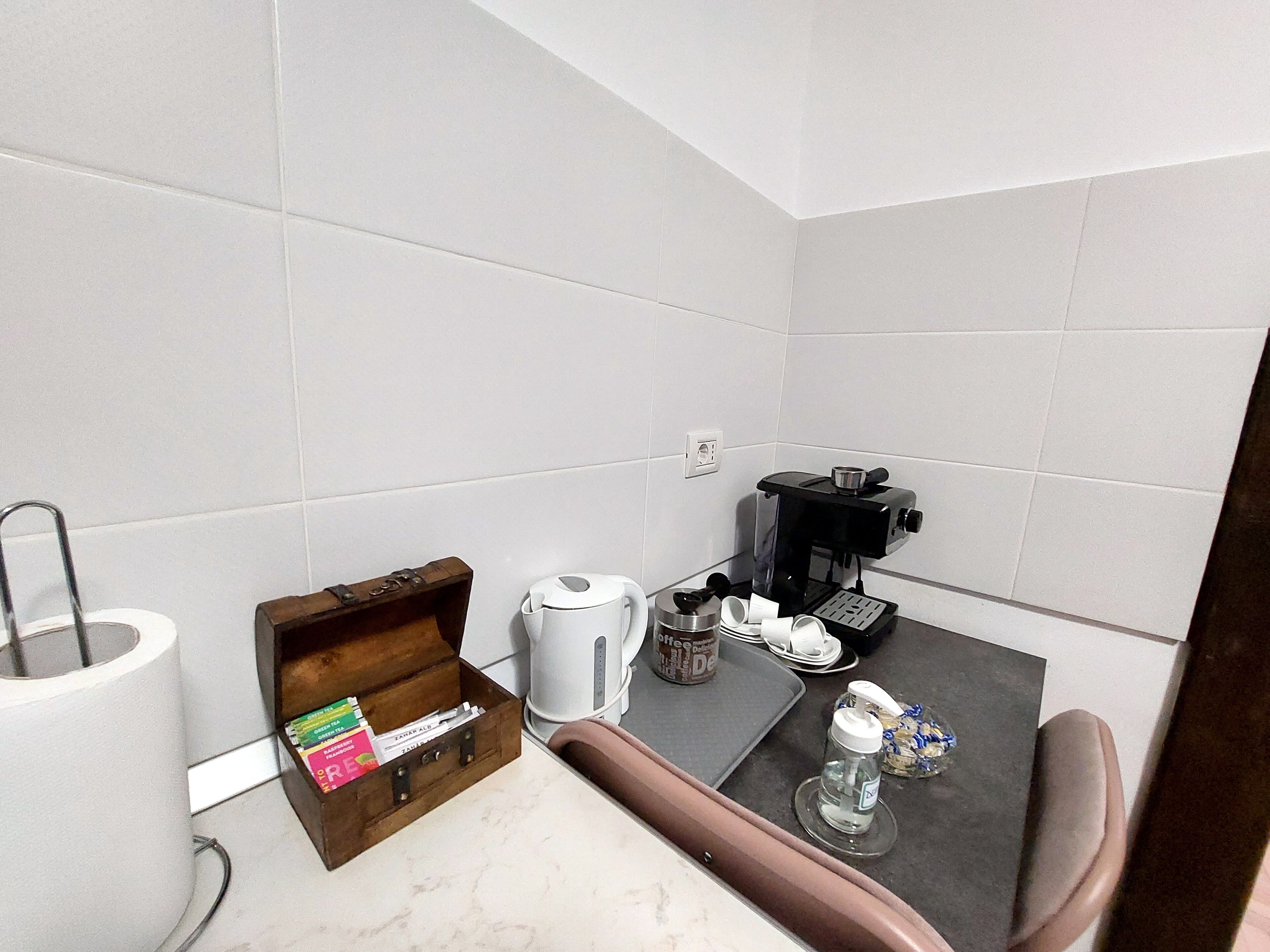 Una pequeña kitchenette equipada con cafetera, hervidor de agua, caja de cápsulas de café y una botella de agua.