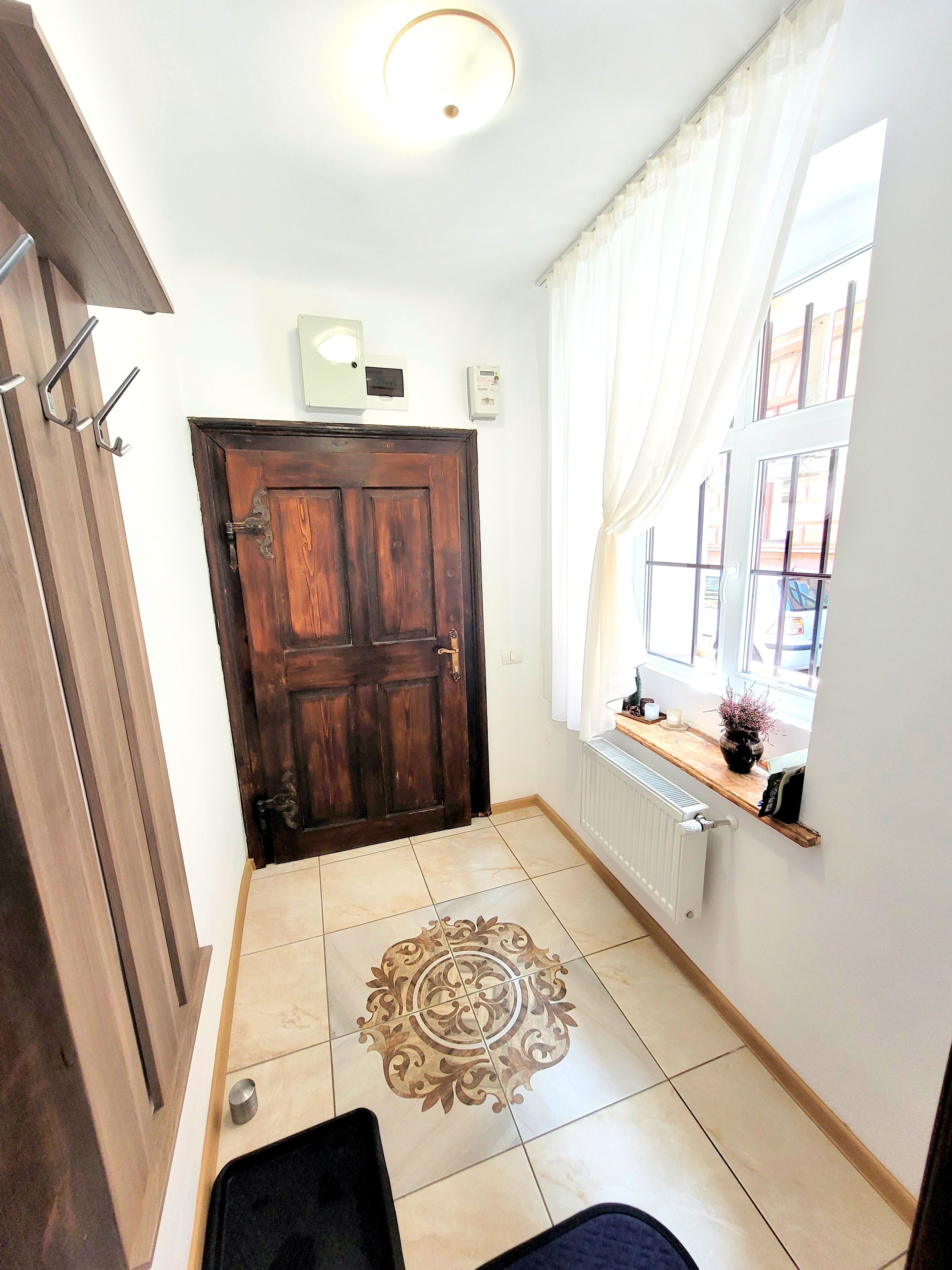 A hallway with a wooden door, a radiator, a window with curtains, and a decorative rug.