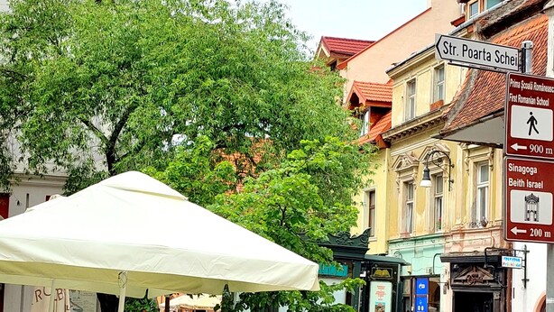 A cobblestone street with a café under a white canopy, surrounded by colorful flower boxes and traditional buildings.