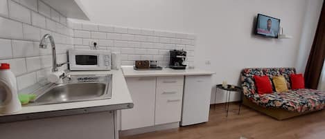 A compact kitchen with white cabinets, a microwave, and a coffee maker. There's a sofa with colorful cushions in the living area.