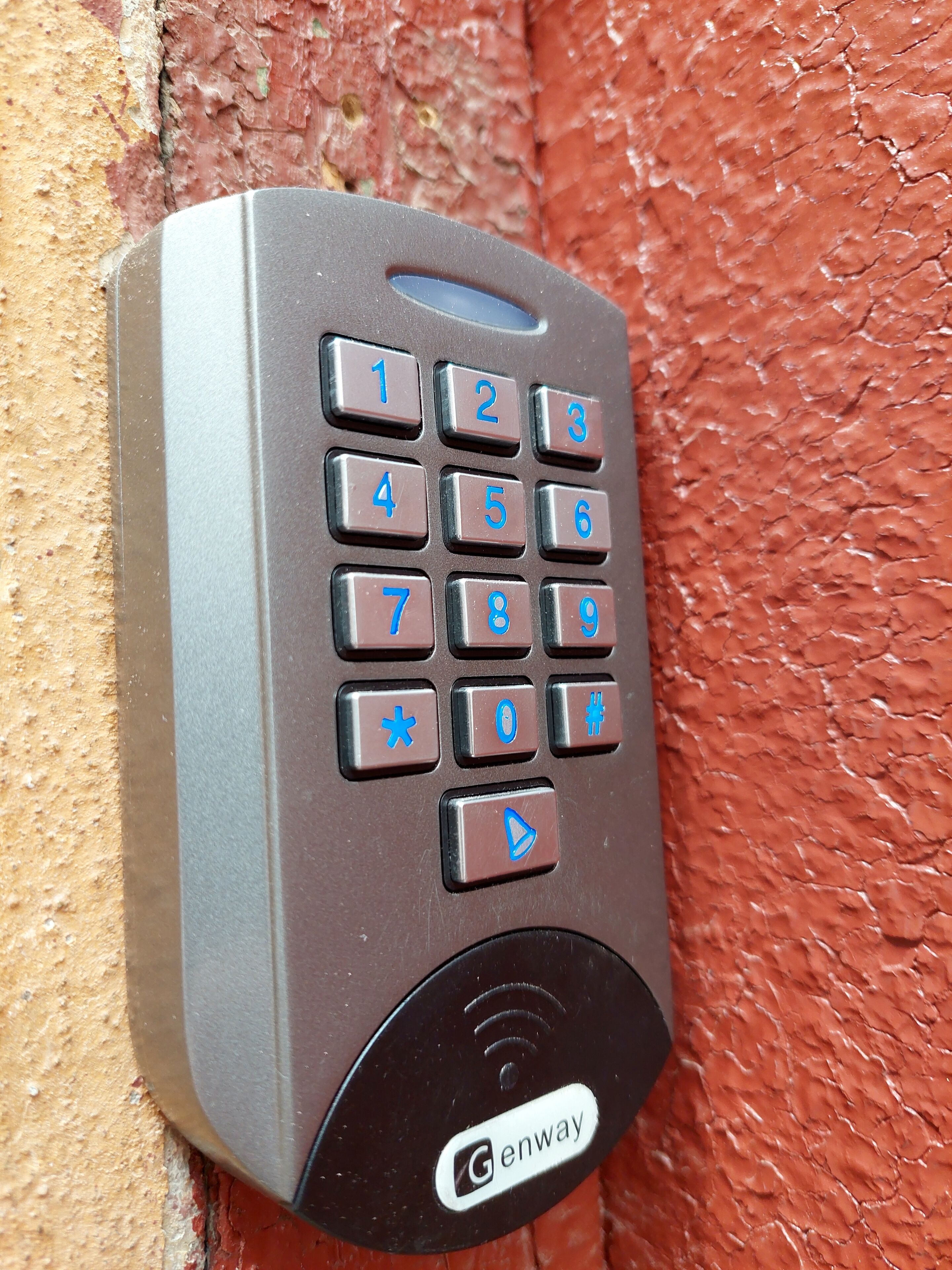 Un dispositivo de intercomunicación marca Genway fijado en una pared roja con textura.
