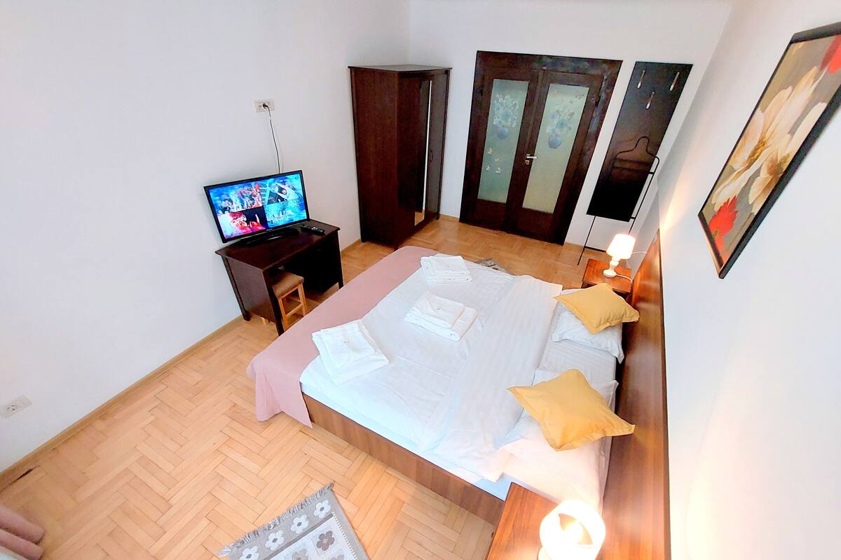 A hotel room with a bed, a desk with a TV, a wardrobe, and a door.